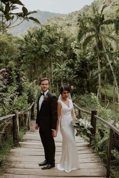 a bride and groom standing on a wooden bridge in the jungle with lush greenery