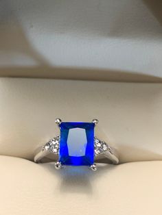 Dazzling blue is a bright color of blue and also the shade of this crystal ring.  This ring has an 8 x 10 mm emerald cut blue crystal on a silver band. The ring is a size 6.5 and is in excellent condition.  I could not find any scratches on the crystal or band.  The large blue crystal has 3 tiny bright crystals on each side. This is a perfect cocktail ring for someone who likes simplicity. Blue Square Cut Topaz Ring, Blue Topaz Ring With Square Cut, Blue Radiant Cut Cubic Zirconia Rings, Blue Sapphire Ring With Square Cut, Dazzling Blue Emerald Cut Ring, Blue Topaz Ring With Square Cut Gemstone, Blue Sapphire Ring With Radiant Cut And Accent Stones, Blue Square Cut Sapphire Promise Ring, Square Cut Blue Sapphire Promise Ring