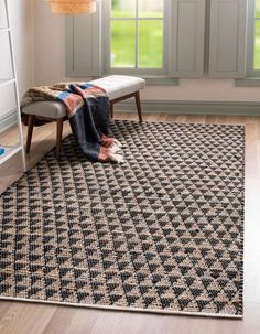 a black and white rug with a bench in front of it on the floor next to a window