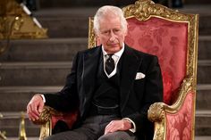 an older man in a suit and tie sitting on a red chair with gold trim