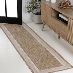 a beige rug on the floor next to a wooden cabinet and vase with plants in it