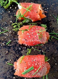 three pieces of salmon with herbs and seasoning on a black surface, ready to be cooked