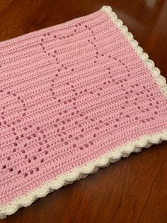 a pink crocheted blanket sitting on top of a wooden floor