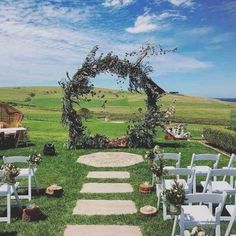 an outdoor ceremony setup with white chairs and greenery on the grass, in front of a grassy field