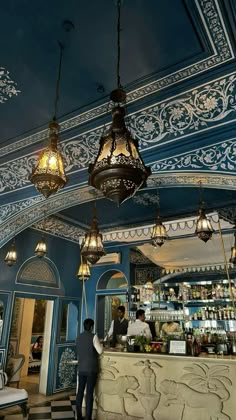 two men are standing at the bar in a blue and white restaurant with chandeliers hanging from the ceiling