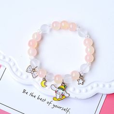 a bracelet with charms on it sitting on top of a pink table next to a card