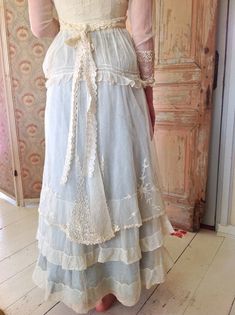 a woman wearing a white dress with ruffles and lace on the skirt is standing in front of a door