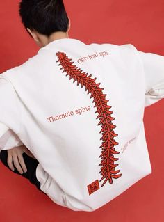 the back of a man wearing a white shirt with red embroidered designs on it and his hands behind his back