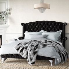 a black and white bedroom with an upholstered bed, fur throw, chandelier and fireplace