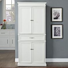 a white cabinet sitting in the corner of a room next to pictures on the wall