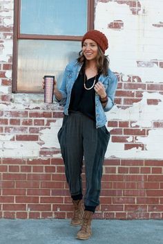 a woman standing in front of a brick building wearing a beanie and black top