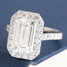 an emerald - cut diamond ring sits on top of a blue book and is surrounded by diamonds