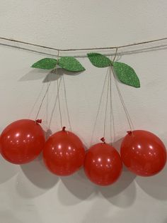 four red balloons hanging from a string with leaves on them and two green leaves attached to the strings