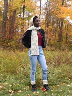 a woman standing in the grass with her hands on her hips and wearing a scarf around her neck