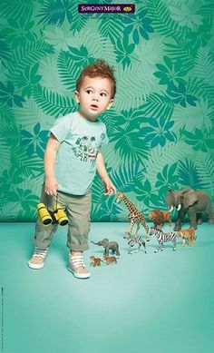 a young boy standing in front of a green wall with toy dinosaurs and giraffes