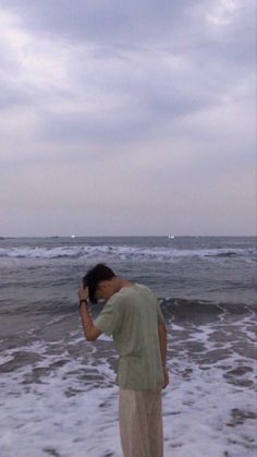 a man standing on top of a beach next to the ocean holding a cell phone