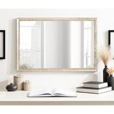 an open book is sitting on a desk in front of a mirror and some vases