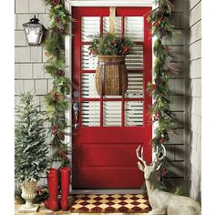 a red front door decorated for christmas with evergreen garland and deer statue next to it