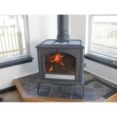 a wood burning stove in the corner of a room with two windows and tile flooring