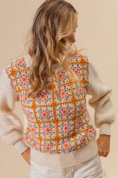 a woman wearing an orange and white crochet sweater with flowers on the back