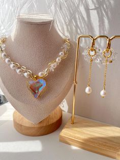 This versatile 2-in`1 necklace features baroque pearls and clear quarz, highlighted by a large heart-shaped pendant with a transparent Swarovski crystal that changes color from blue to yellow. The necklace includes an additional chain, allowing you to wear it as single piece or separately. The necklace measures 38 cm(14.96 inches) with a 5 cm (1.97 inches) extension chain. The earrings, featuring removable pendants, have a diameter of 1.6 cm(0.63 inches) and a total length of 6,5 cm(2.56 inches) Party Jewelry With Pearl And Heart Charm, Pearl Jewelry For Gifts, Clear Pearl Jewelry As A Gift, Clear Pearl Jewelry For Gifts, Heart Pendant Pearl Chain For Party, Party Pearl Chain Jewelry With Heart Pendant, Heart Pendant Pearl Chain Jewelry For Party, Heart Shaped Pearl Chain Jewelry For Party, Elegant Teardrop Heart Beads Jewelry