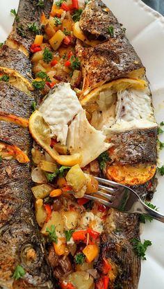 a white plate topped with fish covered in veggies and sauce next to a fork