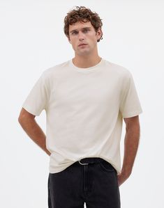 a man standing with his hands in his pockets and wearing a white t - shirt