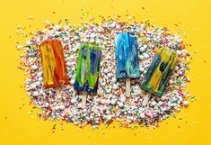 three popsicles with sprinkles on them sitting in front of a yellow background