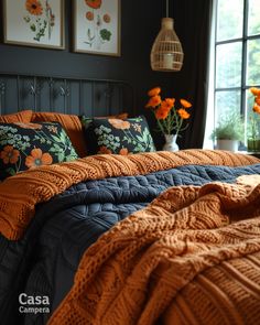 a bed with orange and blue comforters in front of a window filled with potted flowers