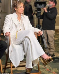 a woman sitting on top of a wooden chair in front of a camera and some people