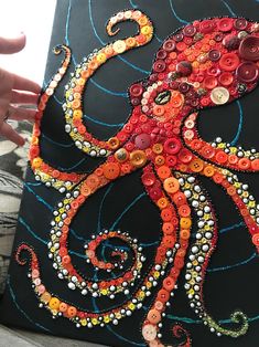 an octopus made out of buttons on a piece of black fabric with white and orange swirls