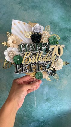 a hand holding up a happy birthday card with flowers and leaves on it, in front of a blue background