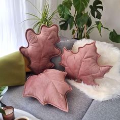 three pink leaf shaped cushions on a grey couch next to a potted plant and coffee cup