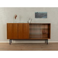 a wooden cabinet with glass doors and shelves on the top, in front of a white wall