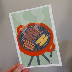 a person holding up a card with an image of a bbq grill