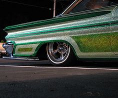 an old green car parked on the side of the road at night with its lights on