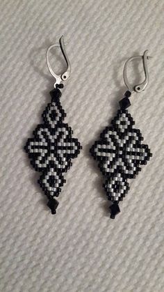 two black and white beaded earrings hanging from silver hooks on a gray fabric surface