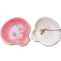 two seashells with pearls on them sitting side by side, one pink and the other white