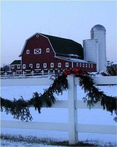 a red barn and white fence decorated with christmas wreaths in front of snow covered fields