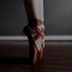 a person's feet in ballet shoes on a wooden floor with dark walls behind them