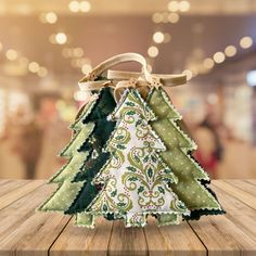 an ornament shaped like a christmas tree on a wooden table with lights in the background