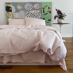 a bed with pink sheets and pillows on top of it in front of a painting