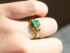 a close up of a person's hand with a gold ring and emerald stone