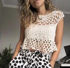 a woman standing in front of a desk wearing a white top with black polka dots