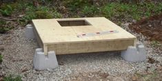 a wooden table sitting on top of a pile of gravel next to trees and bushes