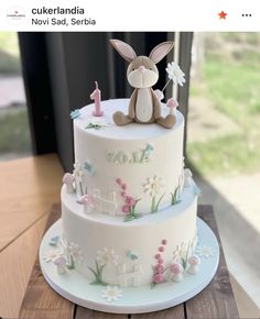 a three tiered cake decorated with flowers and a bunny sitting on top of it