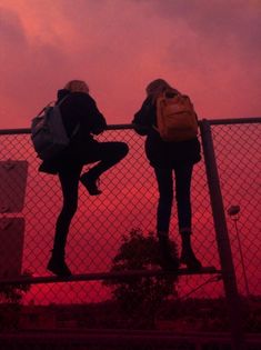 two people standing on a fence with their backs to each other as the sun sets