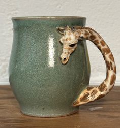 a giraffe's head sticking out of a green mug on a wooden table