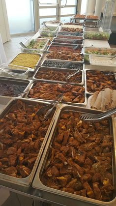 many trays of food are lined up on the buffet table with utensils