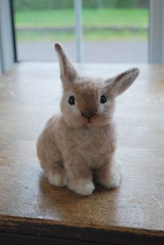 a small stuffed rabbit sitting on top of a wooden table in front of a window